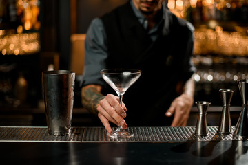 Male bartender holding an emty cocktail glass near steel shaker