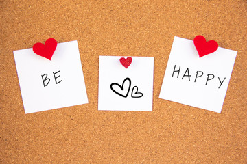 Be happy lettering with hearts on 3 white paper pinned with 2 small red heart pegs and one big red heart pegs on cork board