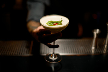 Bartender serving creamy color cocktail decorated with a leaf and red pepper peas