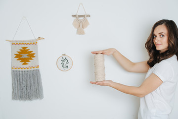 Young woman holding rope coil next to macrame tapestries hanging on the wall