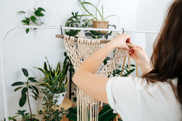 Craftswoman working on unfinished section of a macrame piece at home greenhouse - obrazy, fototapety, plakaty