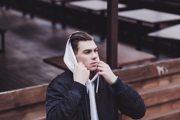 Fototapeta premium portrait of a handsome man in a black jacket and hood in an urban environment