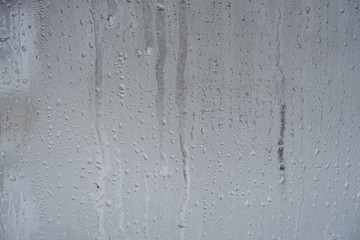 Frozen drops of water on a transparent glass surface on a gray background.