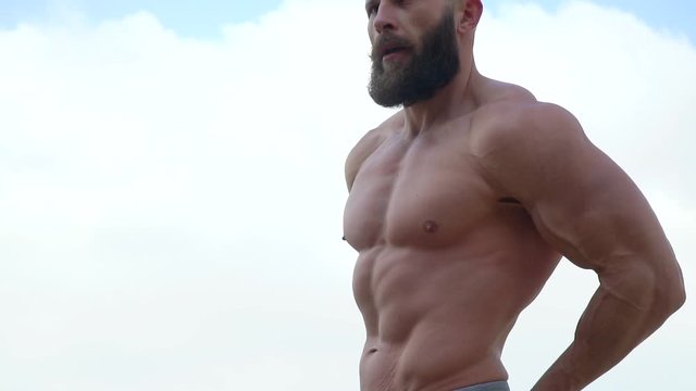 Bodybuilder demonstrates muscles. Young bearded athletic bodybuilder plays sports outdoors