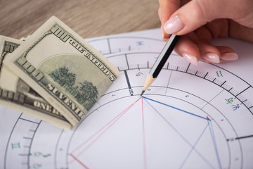 Cropped view of astrologer drawing natal chart beside dollar banknotes on table