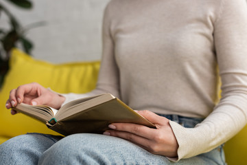 Obraz premium Cropped view of young woman reading book on couch