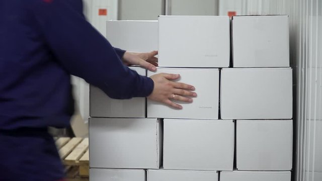 The factory worker carries the cardboard boxes filled from the conveyor and puts them on top of each other