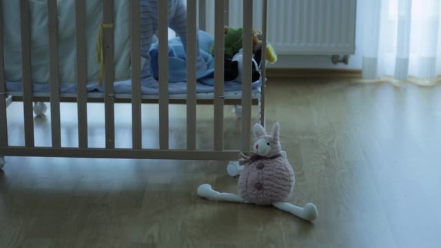 Out of focus of a small kid, child in a wooden baby cot, playing. Lonely. Alone. In the room. Some toys in front of cot.