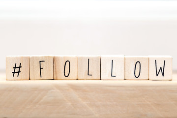 Follow sign made of cubes on a wooden table with Hashtag near white background, socialmedia concept