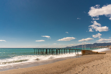 Fototapeta na wymiar Beach, sea and pier in the city of Mahmutlar. Against the blue sky with white clouds
