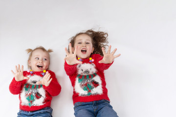Two little girls-sisters in red sweaters-koala and blue jeans, on a white background. The view from the top. The concept of a happy childhood. Blank space for text. Layout for design