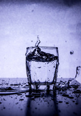 Macro shot of freeze motion of water splash from drinking glass on a white blue background