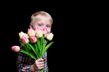 Portrait smiling blond boy with a bouquet of tulips. Black background. Space for text