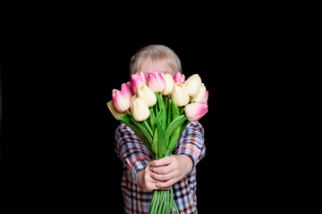 Little boy hides his face behind a bouquet of tulips. Isolate on black background.