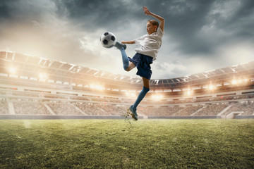 Fototapeta na wymiar Superstar. Young male football or soccer player in sportwear and boots kicking ball for the goal on stadium with flashlights on background. Concept of healthy lifestyle, professional sport, hobby.