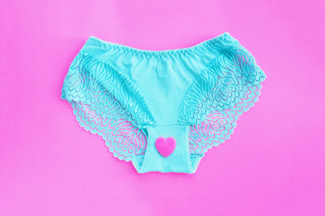 Women's blue lace panties on a bright pink background and a pink heart on panties. The concept of ovulation, menstruation...