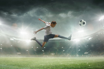 Fototapeta na wymiar Faster than wind. Young male football or soccer player in sportwear and boots kicking ball for the goal on stadium with flashlights on background. Concept of healthy lifestyle, professional sport.