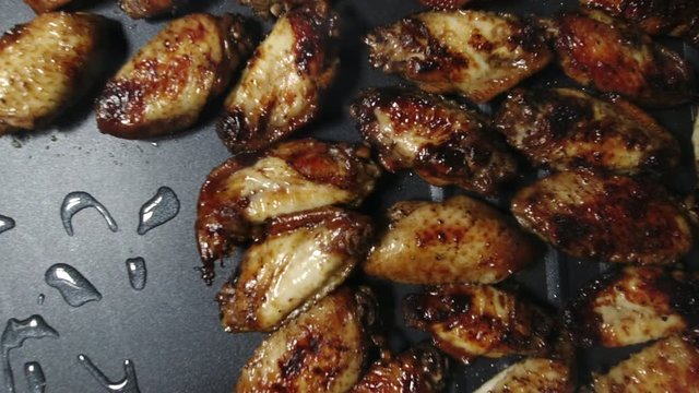 A chef lays chicken wings and red peper on the surface of a hot grill.