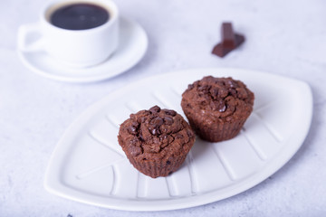 Chocolate muffins on a white plate. Homemade baking. In the background is a cup of coffee. White background. Selective focus, close up.