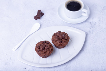Chocolate muffins on a white plate. Homemade baking. In the background is a cup of coffee. White background. Selective focus, close up.