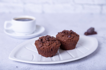 Chocolate muffins on a white plate. Homemade baking. In the background is a cup of coffee. White background. Selective focus, close up.