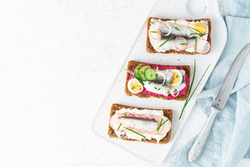 Savory smorrebrod, set of traditional Danish sandwiches. Black rye bread with anchovy, beetroot, radish, eggs, cream cheese on grey plate on white stone table, top view, copy space