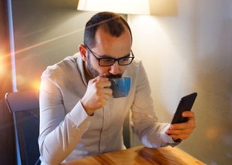 close-up of casual man using smartphone and holding coffee mug and planning reservation over the table