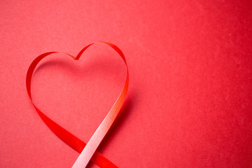Heart made from red gift bow over red background