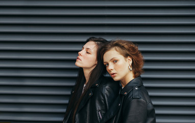 Fashionable portrait of two attractive girls in a leather jacket on a black background, wearing casual clothes, one girl looks in camera with a serious face, other to the side to the empty space.