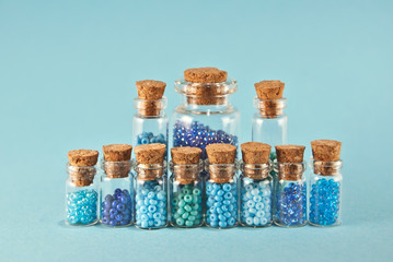 Purple and cyan beads in glass jars on bright blue background. Beads in a transparent container with a wooden cork. The concept of orderliness, balance and chaos.