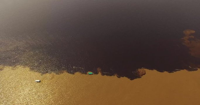 Aerial 4K view over the confluence of the black waters of the Rio Negro with the yellow waters of the Solimoes River. The place from where the Amazon river starts on all maps. Manaus, Brazil.