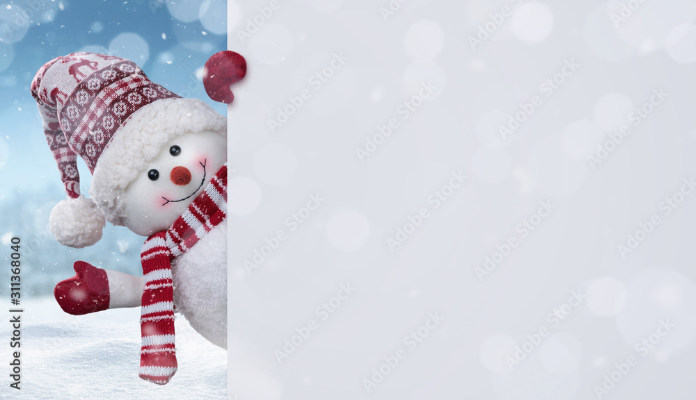 Wall mural happy snowman in the winter scenery behind the blank advertising banner with copy space