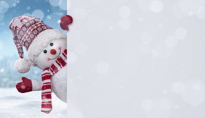 Happy snowman in the winter scenery behind the blank advertising banner with copy space - obrazy, fototapety, plakaty