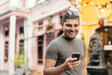Portrait of a young man in green clothes walking down the street, holding a mobile phone and smiling.