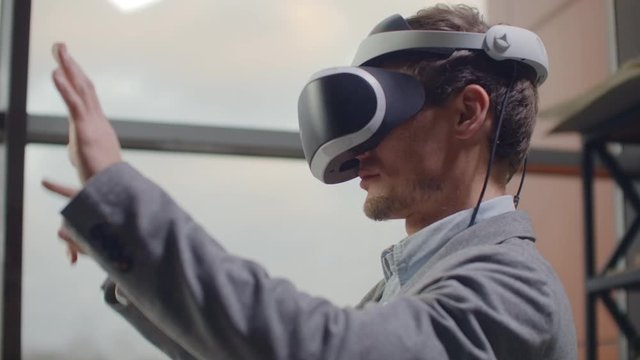 Portrait. male architect-designer in a virtual reality helmet at in a modern office near a large window with his hands imitates the work of interface. Designing the future, the concept of virtual