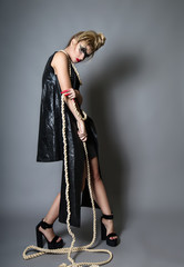 fashion portrait of a girl in a black leather dress with creative make-up and a thick rope in her hands