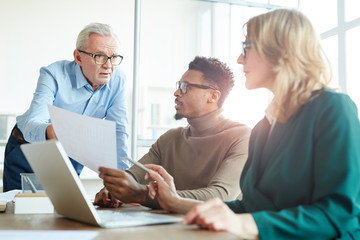 Obraz premium Mature businessman showing document to his colleagues and they discussing it at meeting at office