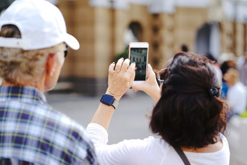 Back view of Senior woman using smartphone for take photos and a senior man are watching, selective focus at senior woman hand