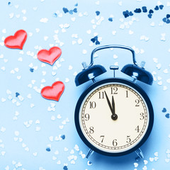 Alarm clock on a blue background with small hearts. The concept of the time of love, the time of date, the wedding, the day of St. Valentine, New Year