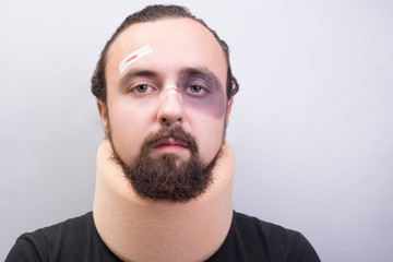 Obraz premium Closeup portrait of a young guy with bruises on his face, with a neck injury. The collar is placed in the neck to immobilize the cervical vertebrae.