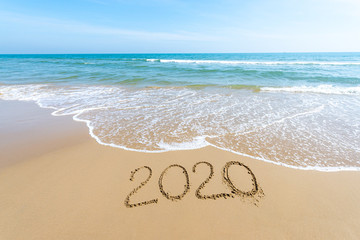 Fototapeta na wymiar Text 2020 Happy New Year on the beach with waves and clear blue sea. 2020 numbers on the coast. Hand written messages in sand on a beautiful beach background