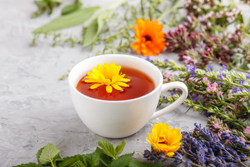 Cup of herbal tea with calendula, lavender, oregano, hyssop, mint and lemon balm on a gray concrete background. Side view, selective focus.