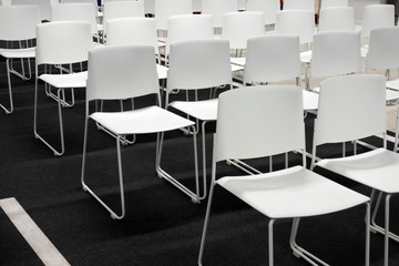 Rows of white plastic chairs for formal meetings, conference, lectures, graduation ceremonies. Room full of empty white chairs.
