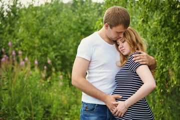 Young happy couple in love outdoors. loving man and pregnant woman in a park.