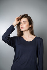 young beautiful girl with long brown hair. She raised her hand to her hair. Dark blue sweatshirt. Grey background