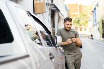 Portrait of a young man in green clothes with a mobile phone in his hand near a car on a summer...