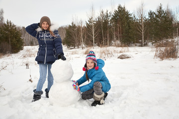 Fototapeta na wymiar two female friends building a snowman. funny girls on a walk in the winter outdoors.