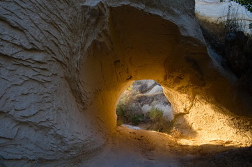 Sunlit way under the rocky mountain. Small cave with gold sunlight on sunset. Cappadocia, Turkey