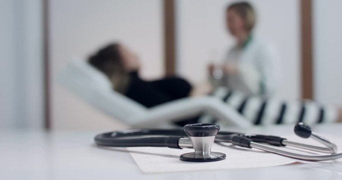 Closeup of stethoscope on the electrocardiogram (EKG). Doctor and Patient blurred background. Tracking shot