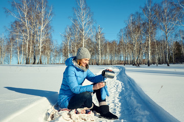woman on a walk in the winter forest drinking tea from a thermos.